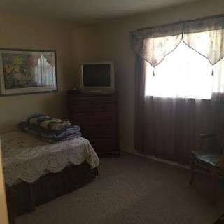 A cozy bedroom featuring a bed, dresser, and a window dressed with curtains.