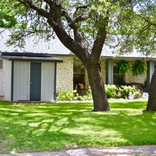 A suburban house with a well-maintained garden and trees in the front yard.
