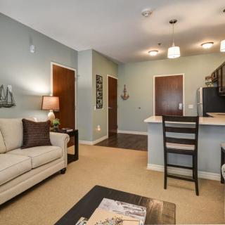 A modern apartment living room with an open concept design, featuring a comfortable sofa, kitchen counter, and stylish ceiling lights.