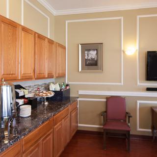 A small kitchen area with wooden cabinets, a coffee station, and a wall-mounted TV.