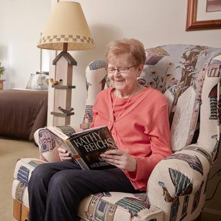 An elderly woman enjoys reading a book while sitting in a cozy armchair in the living room.