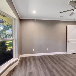 An empty room featuring wood flooring, a large window, ceiling fan, and door.