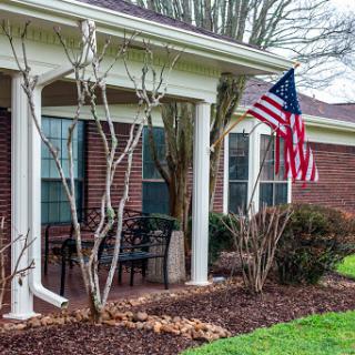 A welcoming house with a front porch featuring an American flag and well-maintained landscaping.
