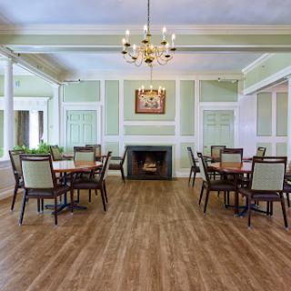 A spacious and elegantly designed dining room featuring wooden furniture, a cozy fireplace, and a chandelier.