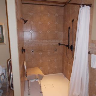 An accessible bathroom with a shower featuring grab bars, a shower chair, and tiled walls.