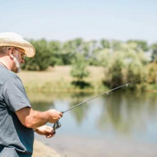 A person wearing a hat is fishing by a calm lake.