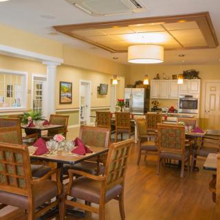 A cozy dining area with neatly arranged tables and chairs, adjacent to a kitchen space.