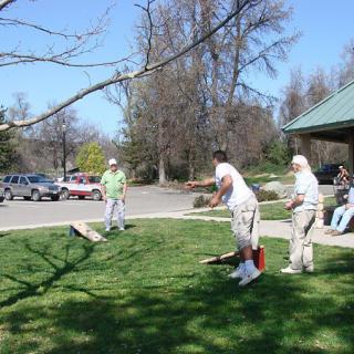 A group of people playing cornhole in a park on a sunny day.