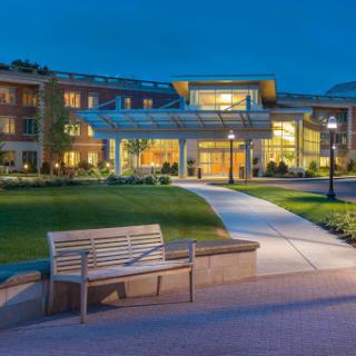 A beautifully illuminated building at dusk, featuring a well-maintained pathway and bench in a serene outdoor setting.