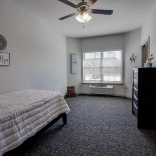 A minimalist bedroom with a single bed, window, dresser, and ceiling fan.