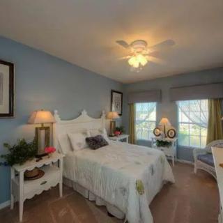 A cozy bedroom with blue walls, white furniture, and a ceiling fan.