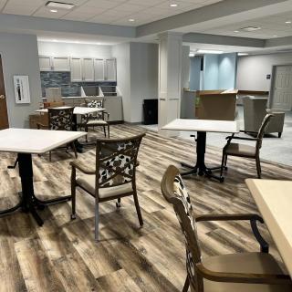A modern seating area with tables and chairs, featuring a kitchenette in the background.