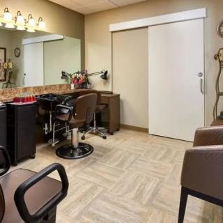 A cozy and well-arranged hair salon interior with chairs, a large mirror, and ample lighting.