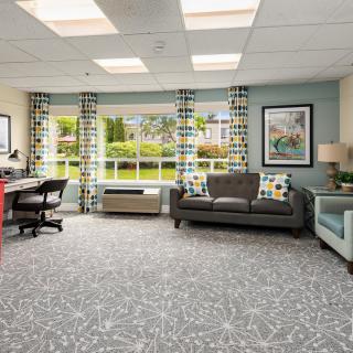 A cozy living room and office space with modern furniture, large windows, and patterned decor.