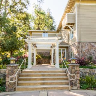 A welcoming house entrance with stairs and lush landscaping on a sunny day.