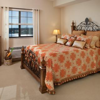 A cozy bedroom with a large wooden bed featuring floral bedding, matching pillows, and a warm lamp by the side.