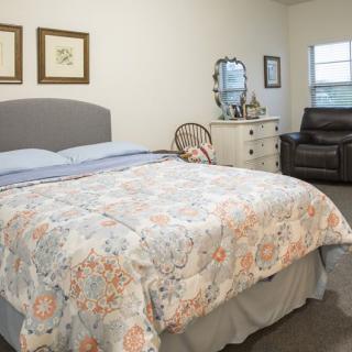 A cozy bedroom with a floral bedspread, dresser with mirror, and comfortable seating.