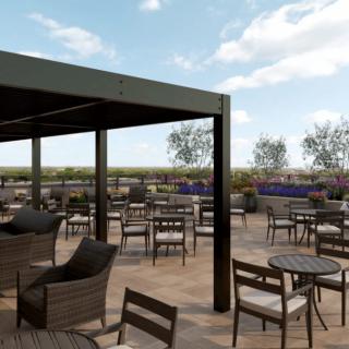 An outdoor restaurant terrace with tables and chairs under a pergola, surrounded by plants.