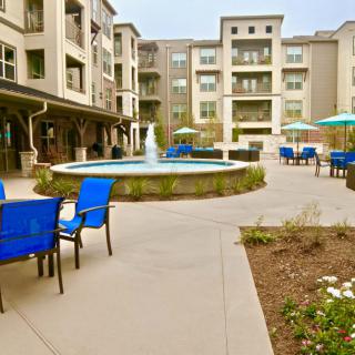A modern apartment complex courtyard featuring a central fountain and blue outdoor seating.