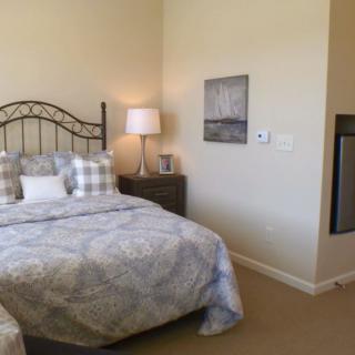 A cozy bedroom featuring a metal-framed bed with patterned bedding, a nightstand with a lamp, and wall art.