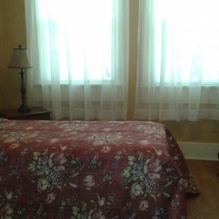 A cozy bedroom with a floral bedspread, bedside lamp, and sheer curtains.
