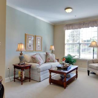 A cozy and well-lit living room with a sofa, coffee table, lamps, and artwork on the walls.