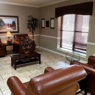 A cozy waiting room with brown leather chairs, a small wooden table, and a decorative lamp under a warm painting.