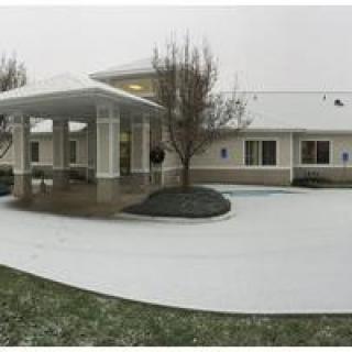A snowy driveway leads to a building entrance surrounded by winter trees on an overcast day.