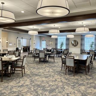 A spacious dining room with multiple tables and chairs, featuring elegant lighting and decor.