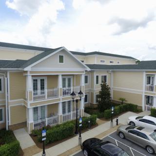 A view of a residential apartment building with a parking lot in front, under a cloudy sky.