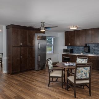 A modern kitchen and dining area featuring wooden flooring, dark cabinets, and a round dining table with chairs.