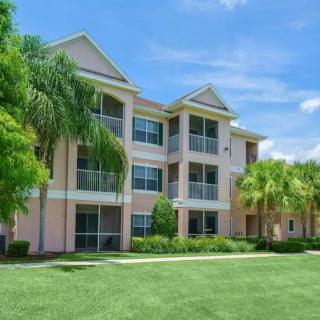 A modern apartment building surrounded by palm trees and greenery on a sunny day.