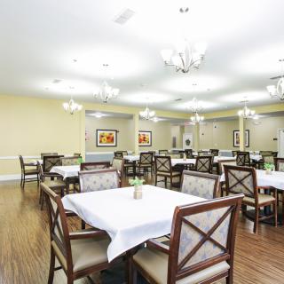 A spacious dining room with elegantly arranged tables and chairs, featuring bright lighting from chandeliers.