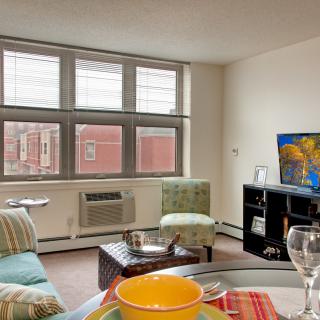 A cozy living room in an apartment with a large window, television, and comfortable seating.
