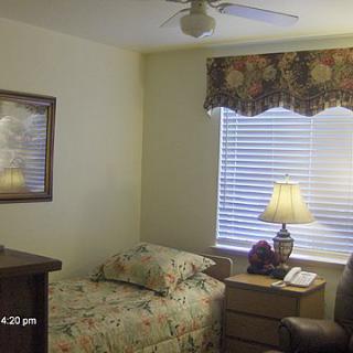 A cozy bedroom with a single bed, bedside lamp, and window covered by floral curtains.