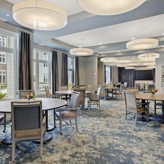 A modern conference room with round tables and chairs, featuring large lighting fixtures and a carpeted floor.