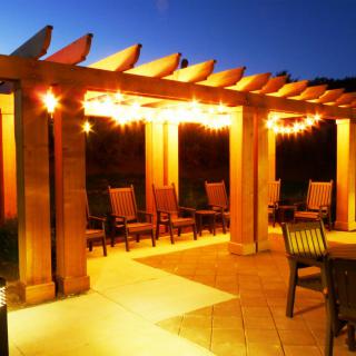 A well-lit outdoor pergola with chairs on a patio at night.