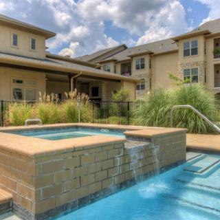A residential building with a pool and spa, surrounded by landscaping under a partly cloudy sky.