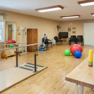 A well-equipped physical therapy room with balance bars, exercise balls, and other gym equipment.