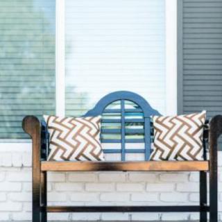 A stylish outdoor bench with patterned pillows in front of a window.