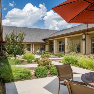 A tranquil outdoor patio area with modern landscaping, featuring a seating arrangement under an orange umbrella.
