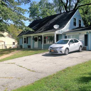 A residential house with a car parked in the driveway and surrounded by trees.