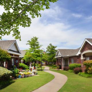 A picturesque view of cottages surrounded by lush greenery with a winding pathway under a clear blue sky.