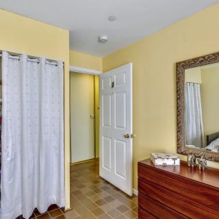 A cozy bedroom with yellow walls, featuring a dresser with a mirror above and a doorway leading to a hallway.