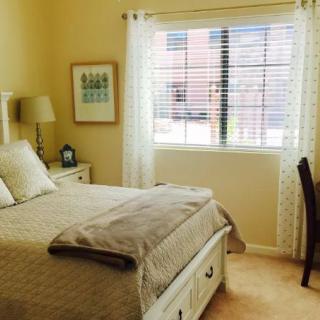 A cozy bedroom with a bed, lamp, window, and chair.