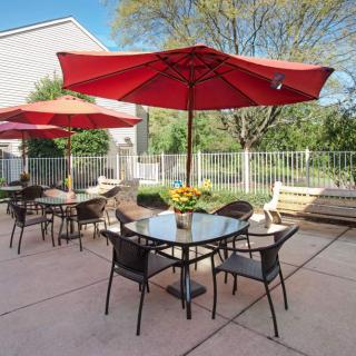 An inviting outdoor patio with tables, chairs, and vibrant red umbrellas set under a clear blue sky.