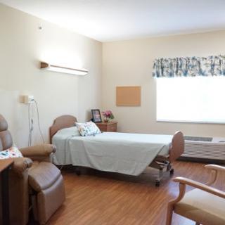 A well-lit and organized patient room in a hospital, featuring a bed, seating area, and window.