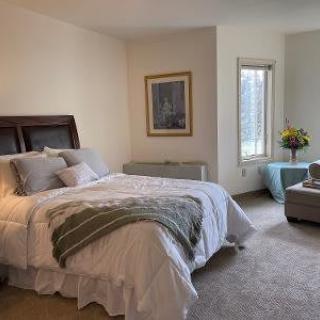 A cozy bedroom with a large bed, armchair, and window providing natural light.