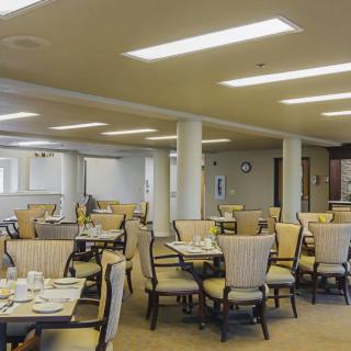 A spacious dining room with neatly arranged tables and chairs, well-lit by overhead lights.