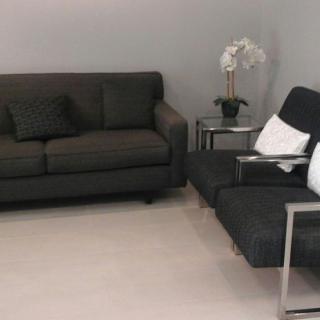 A modern living room featuring a dark sofa and armchair with a side table and decorative indoor plant.